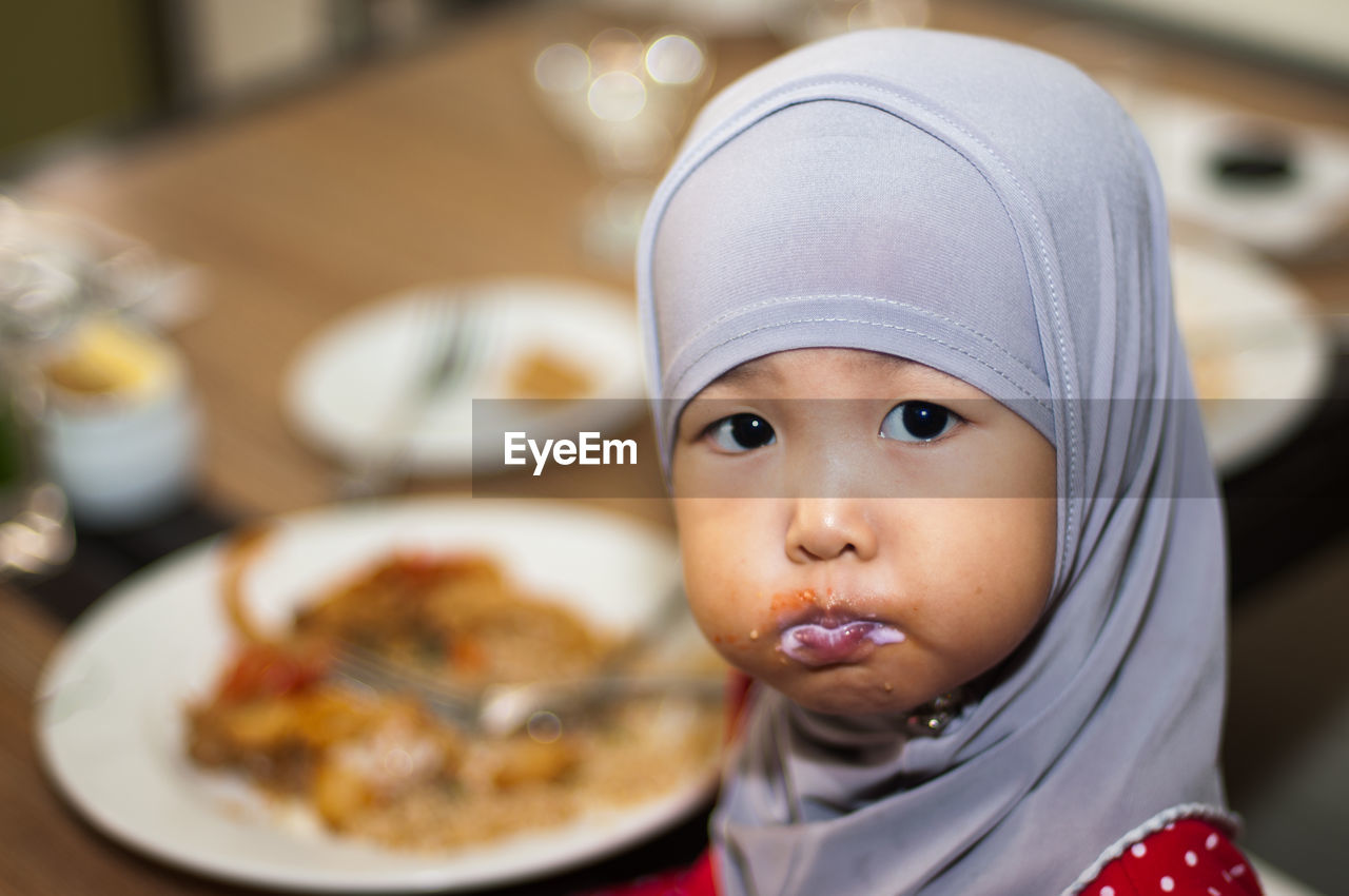 Portrait of girl wearing hijab while mouth filled with food at restaurant