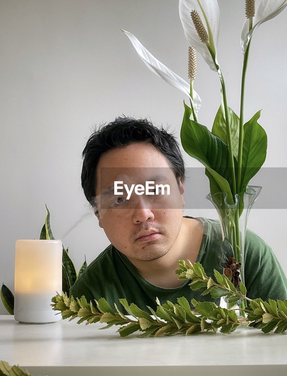 Portrait of young asian man with aromatherapy diffuser, peace lilies, branches on white background 