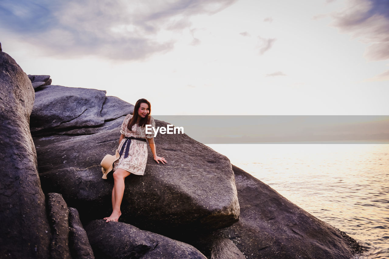 FULL LENGTH OF YOUNG WOMAN ON ROCK AT BEACH