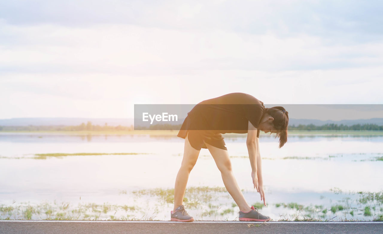 Woman exercising against lake at sunset