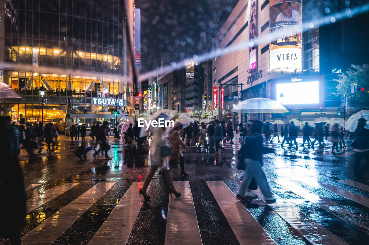 Crowd walking on street during rainy season in city at night