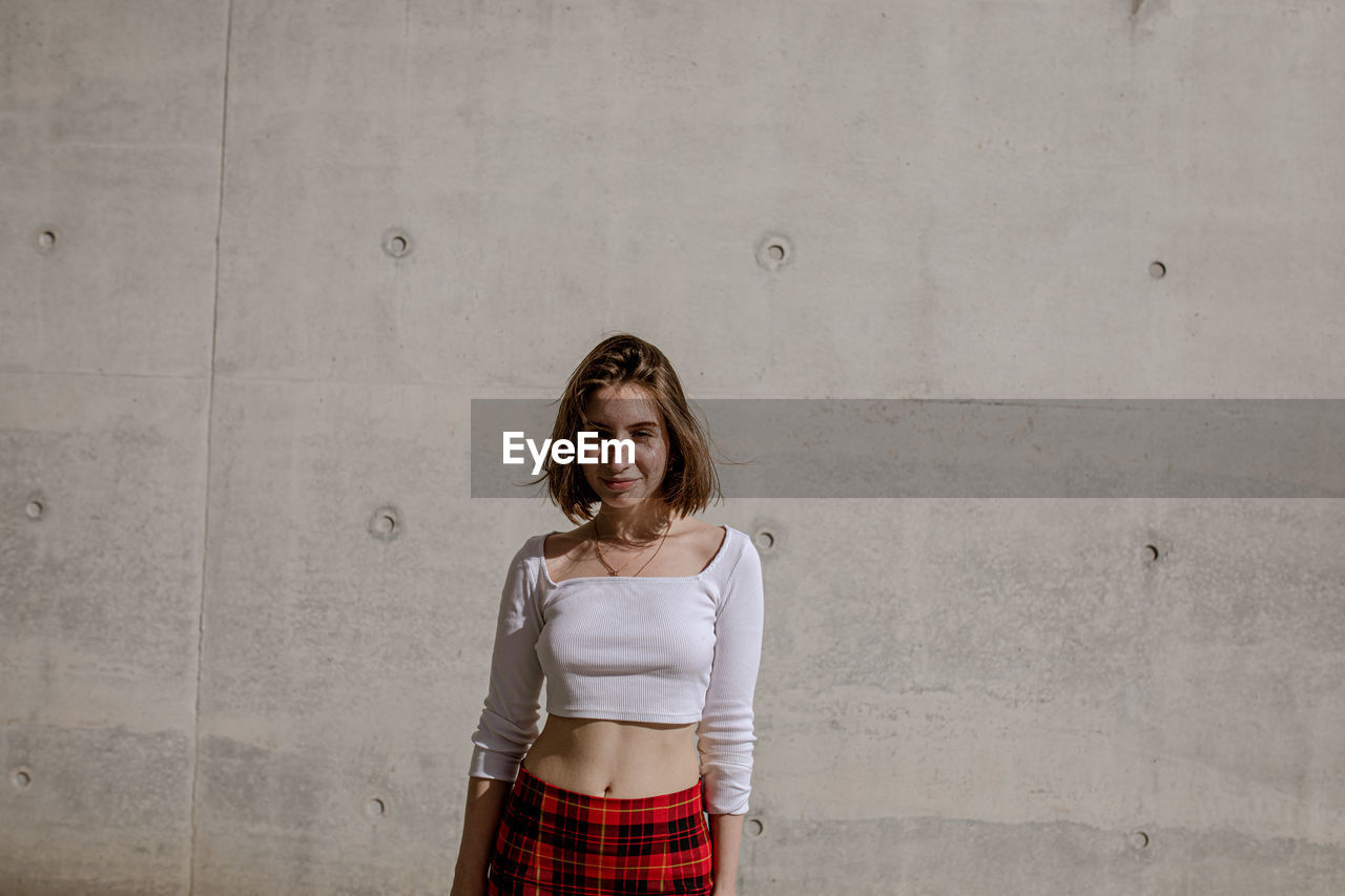 Portrait of smiling young woman standing against wall