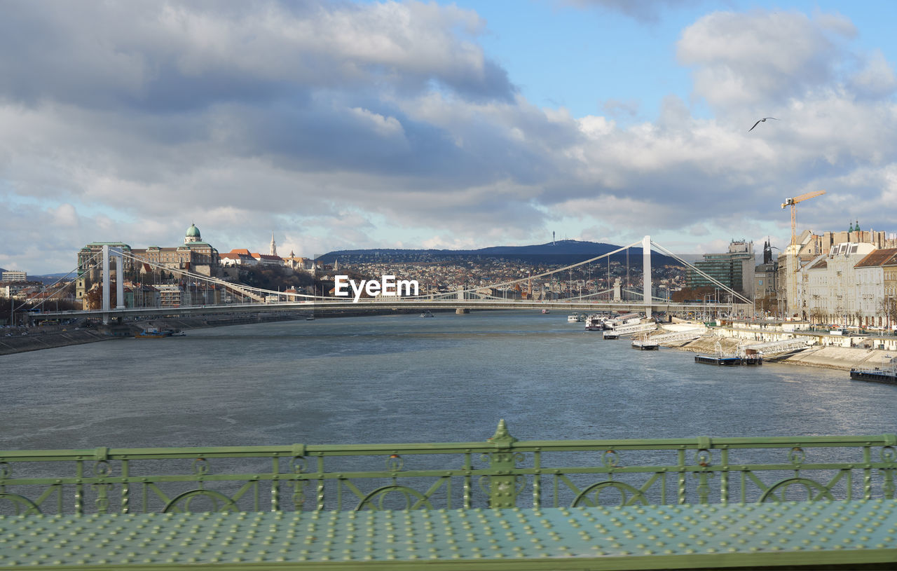 Bridge over river in city against cloudy sky