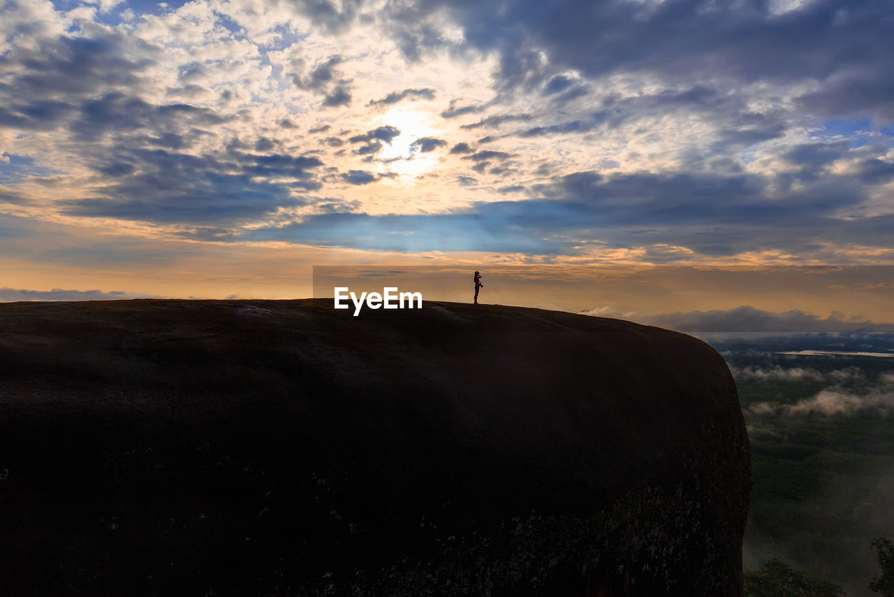 Mid distance of silhouette woman standing on mountain against cloudy sky during sunset