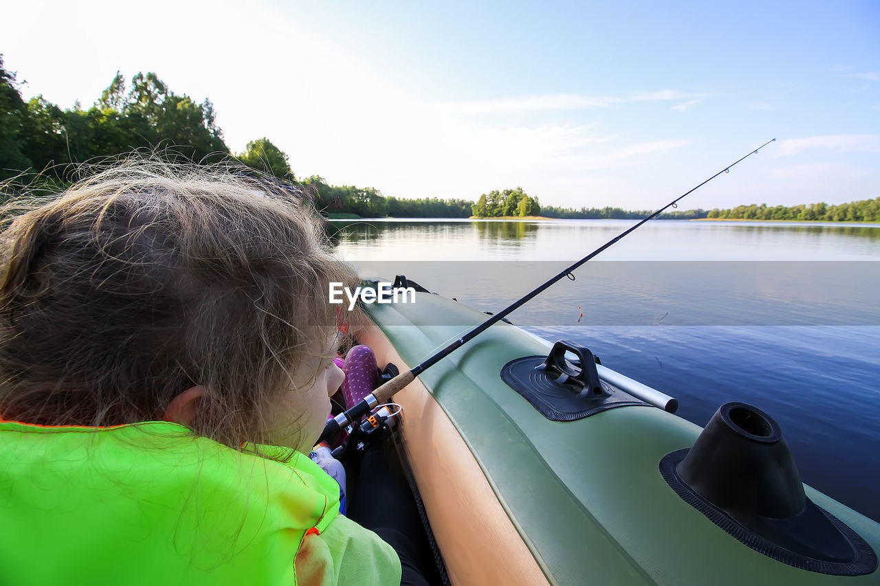 REAR VIEW OF WOMAN FISHING IN LAKE AGAINST SKY