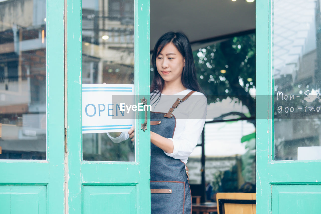 Female owner putting open sign on door in cafe