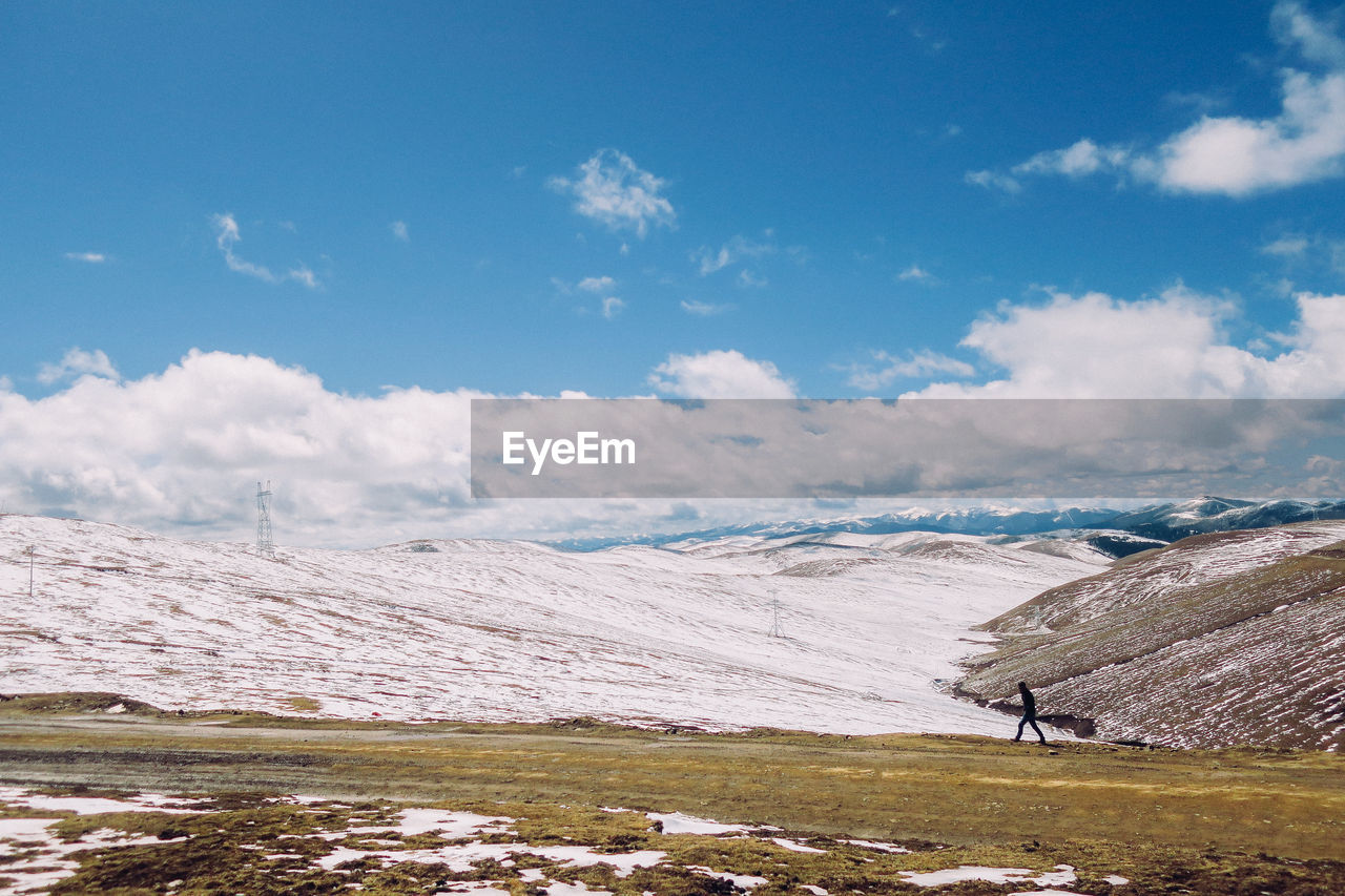 Distant view of man walking on landscape against sky during winter