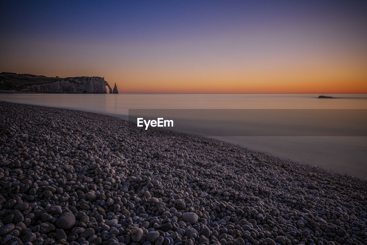 horizon, sky, water, sea, sunrise, dawn, scenics - nature, land, beauty in nature, beach, ocean, nature, tranquility, shore, coast, morning, tranquil scene, horizon over water, reflection, wave, sand, sunlight, no people, environment, seascape, landscape, cloud, idyllic, outdoors, clear sky, orange color, travel destinations, body of water, non-urban scene, coastline, travel, sun, blue, rock