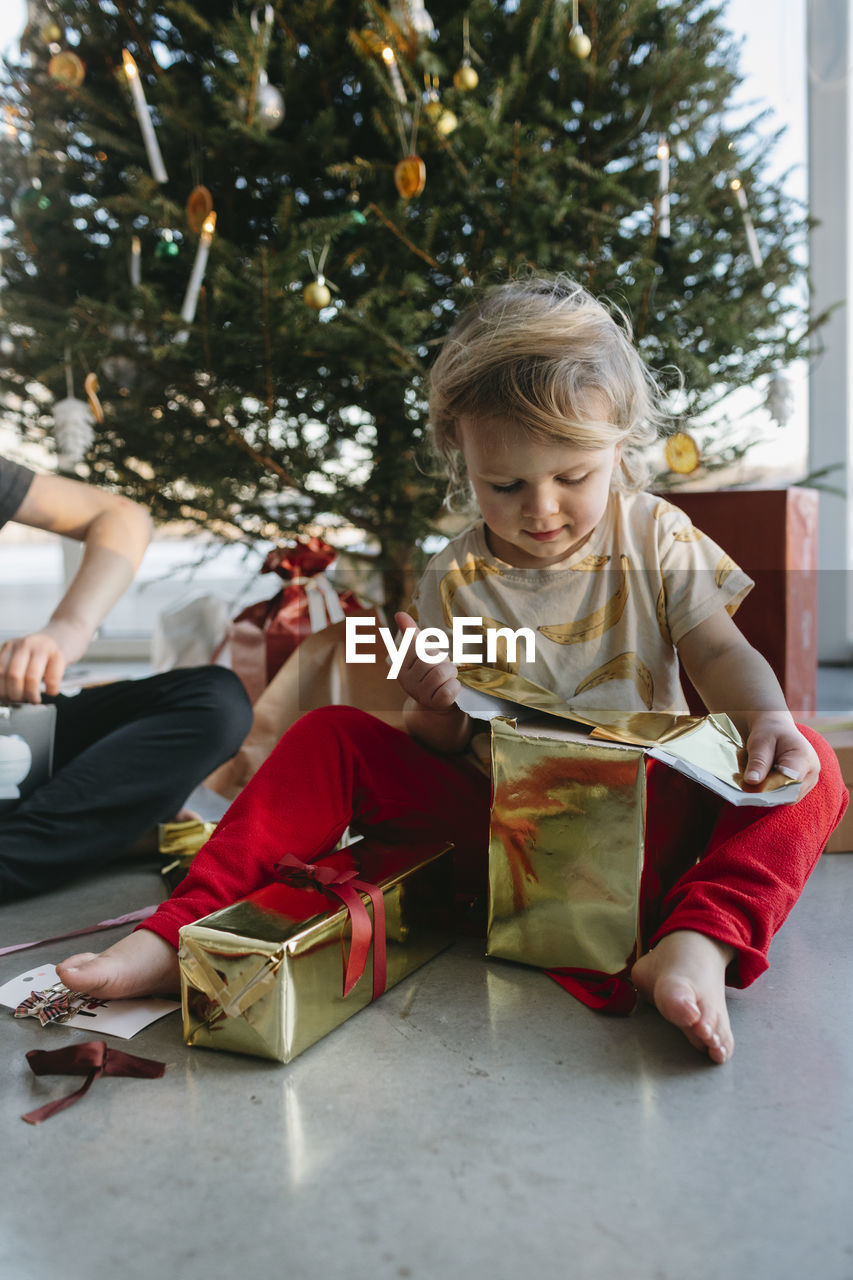 Girl opening christmas presents under christmas tree  barefoot