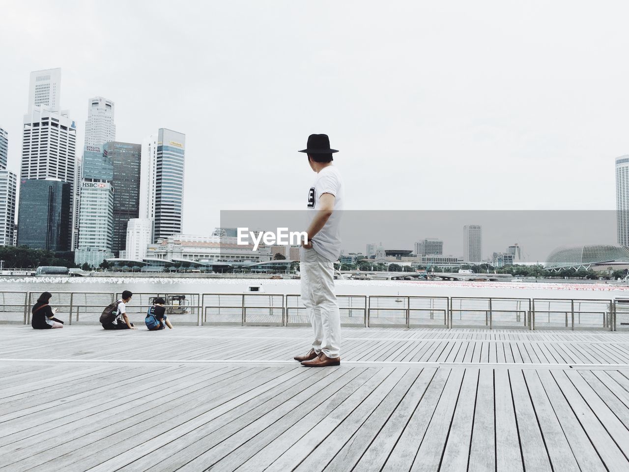 Side view of man standing on boardwalk by river in city against sky