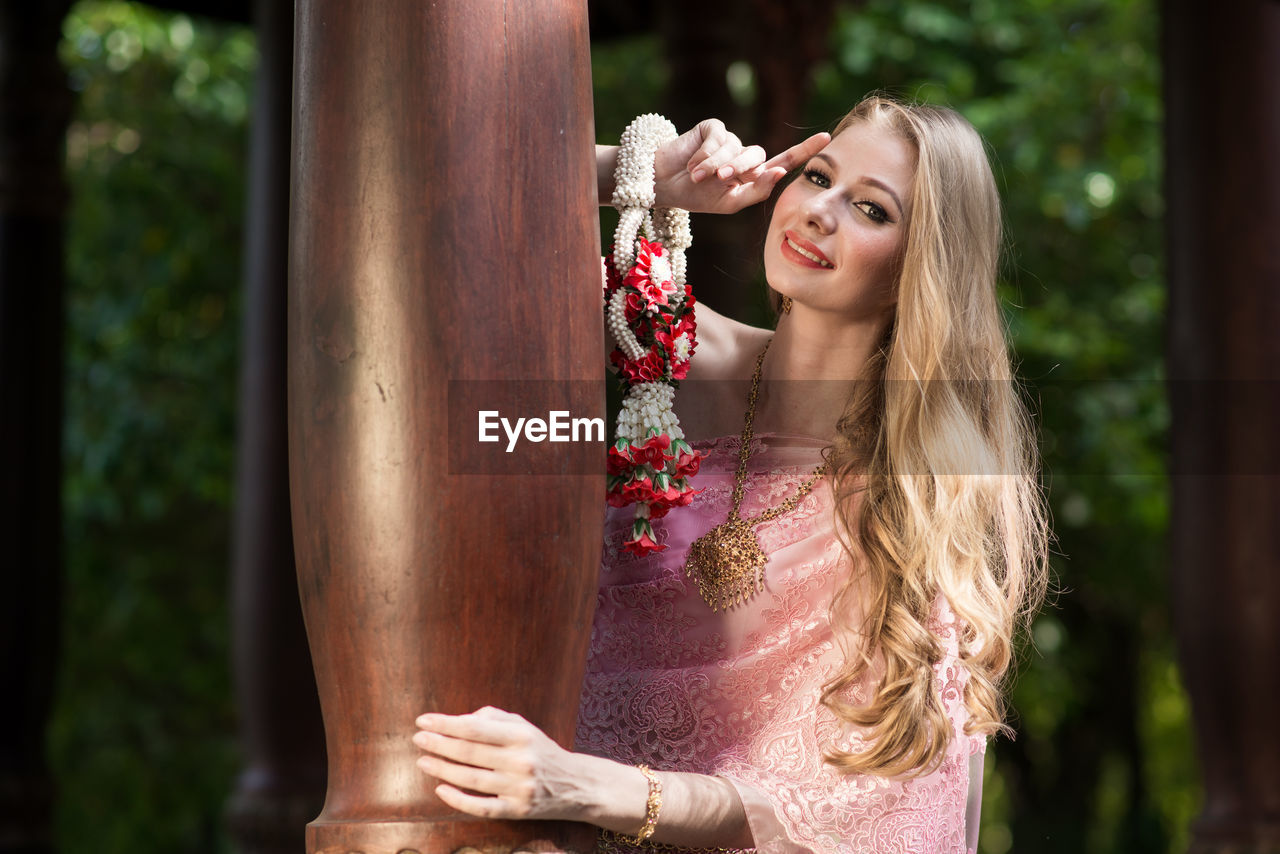 PORTRAIT OF YOUNG WOMAN STANDING BY PLANT