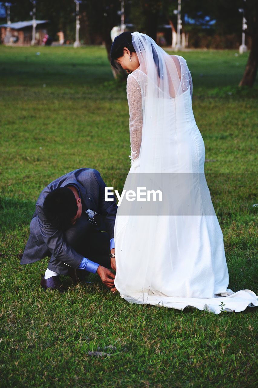 Groom adjusting bride sandal on field