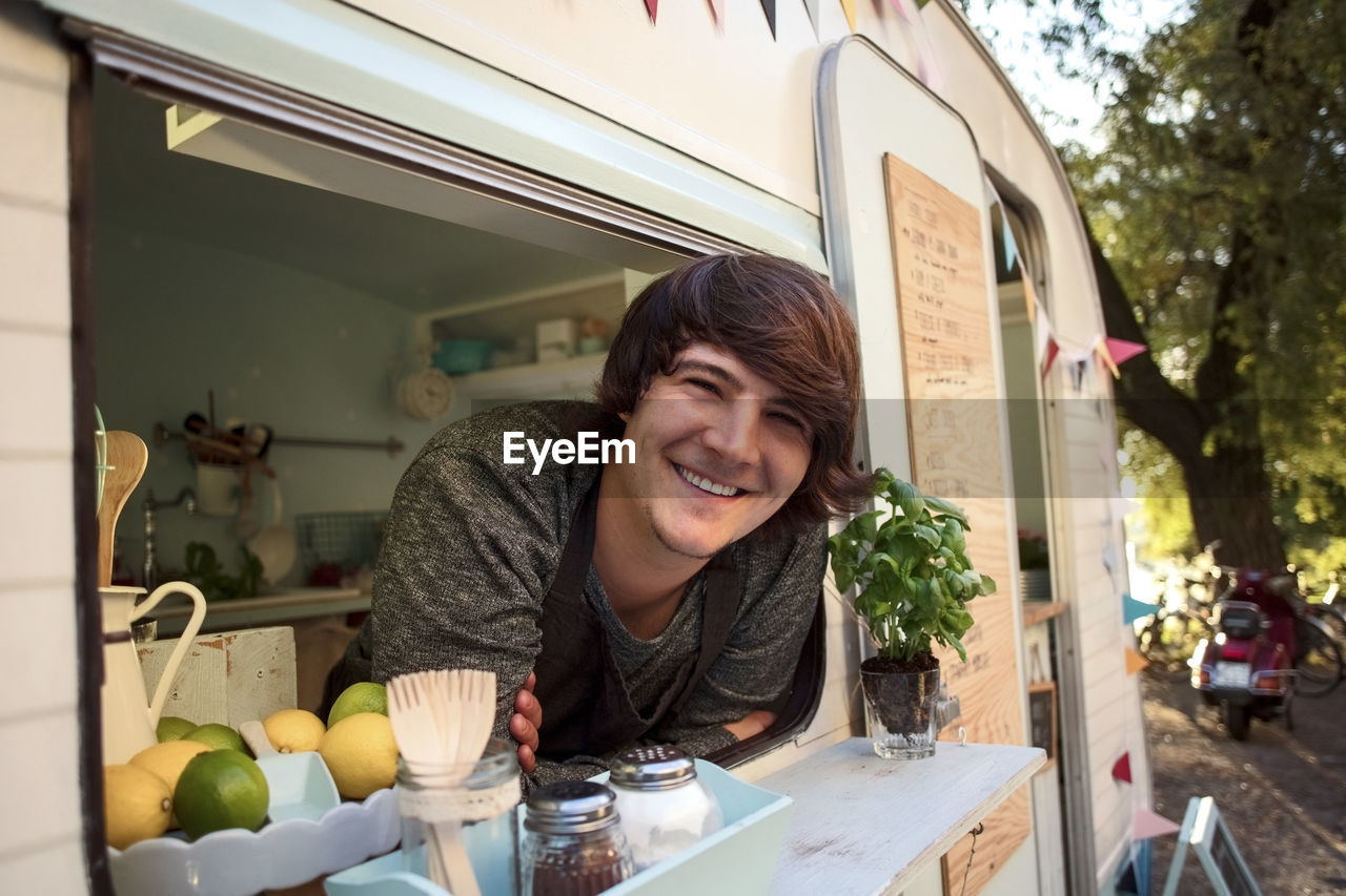 Portrait of happy male owner leaning on food truck window