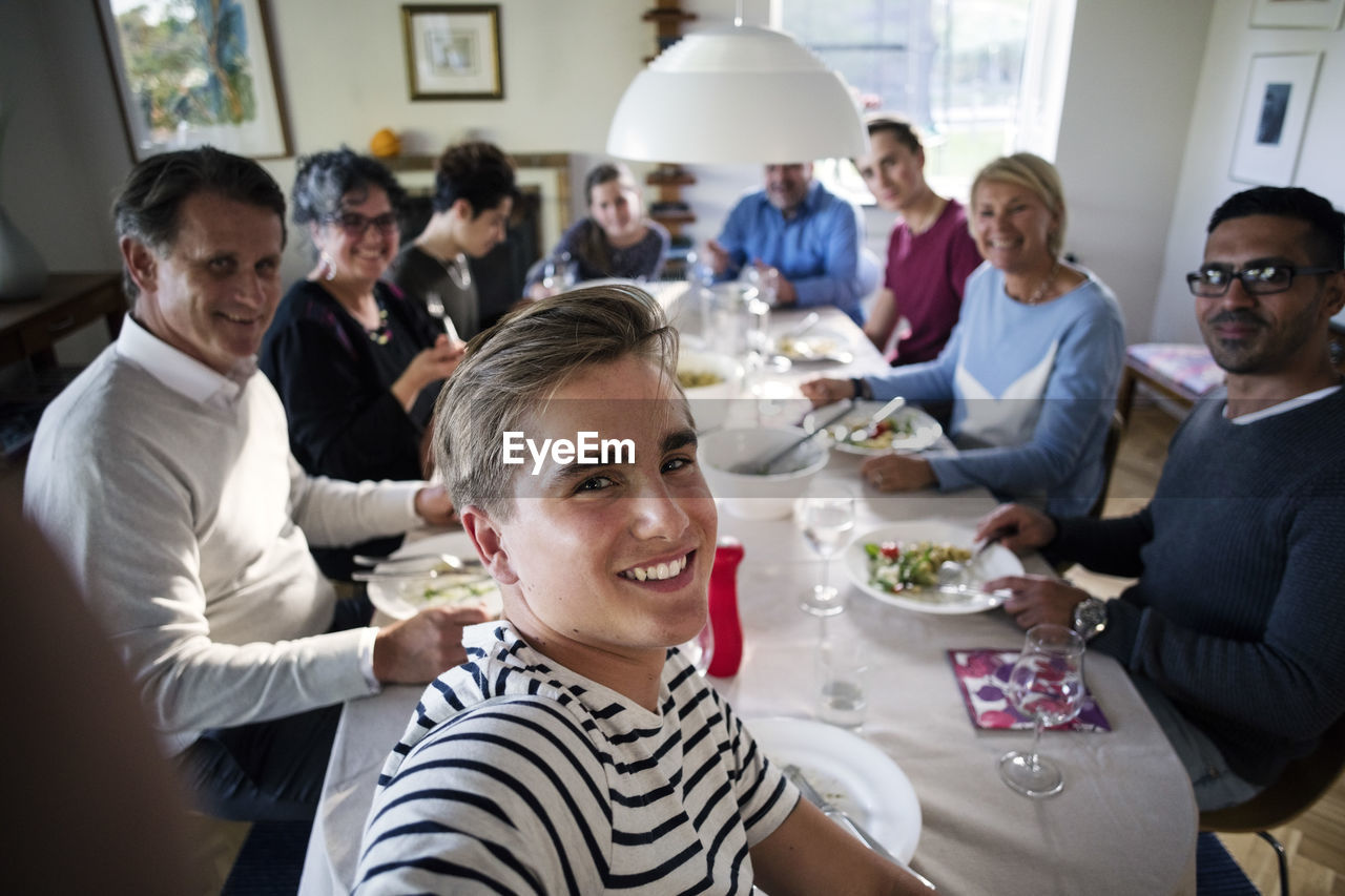 High angle view of smiling teenage boy taking selfie with family and friends at dining table