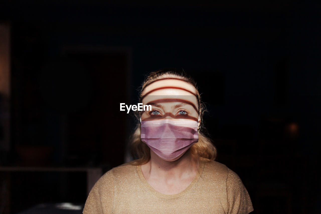 Portrait of young woman wearing mask in darkroom