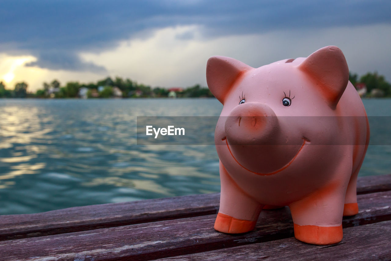 Close-up of piggy bank on table at lake against sky