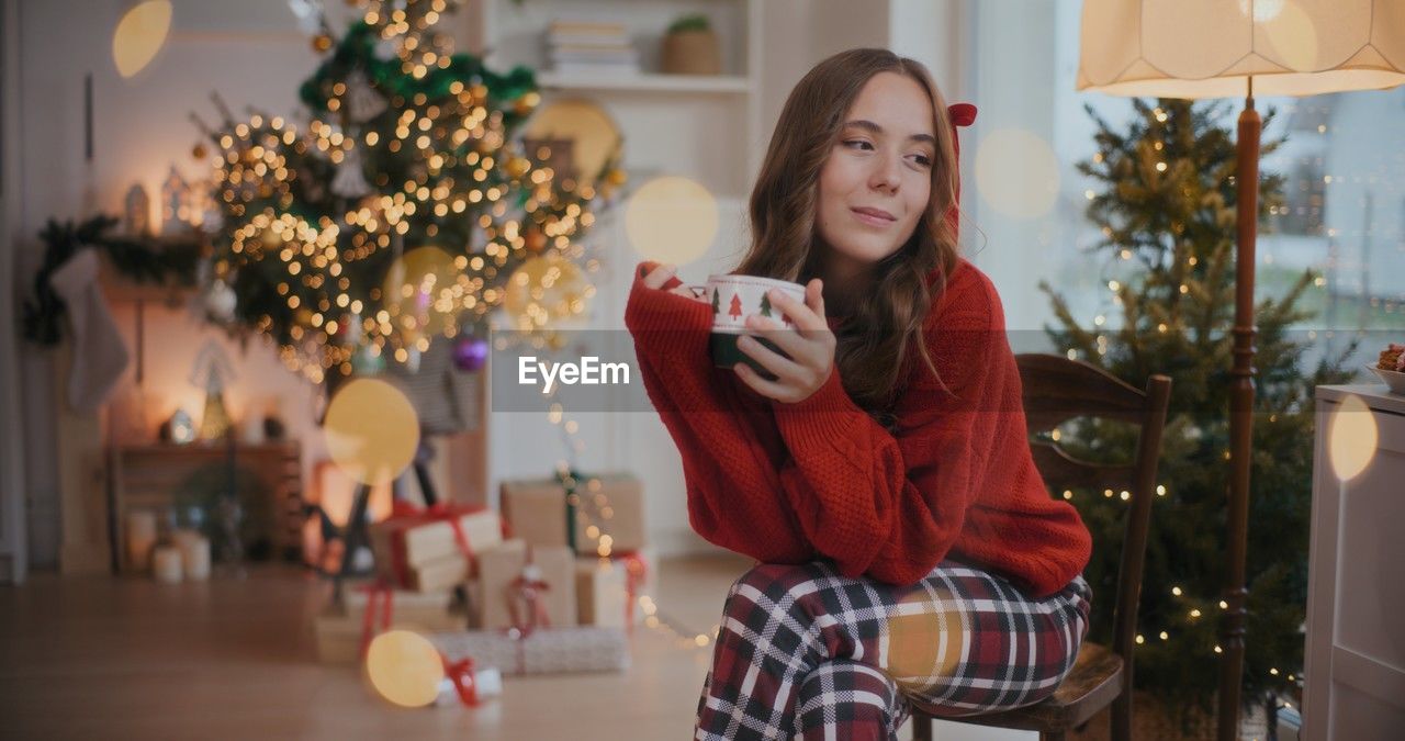 portrait of young woman using mobile phone while standing against christmas tree