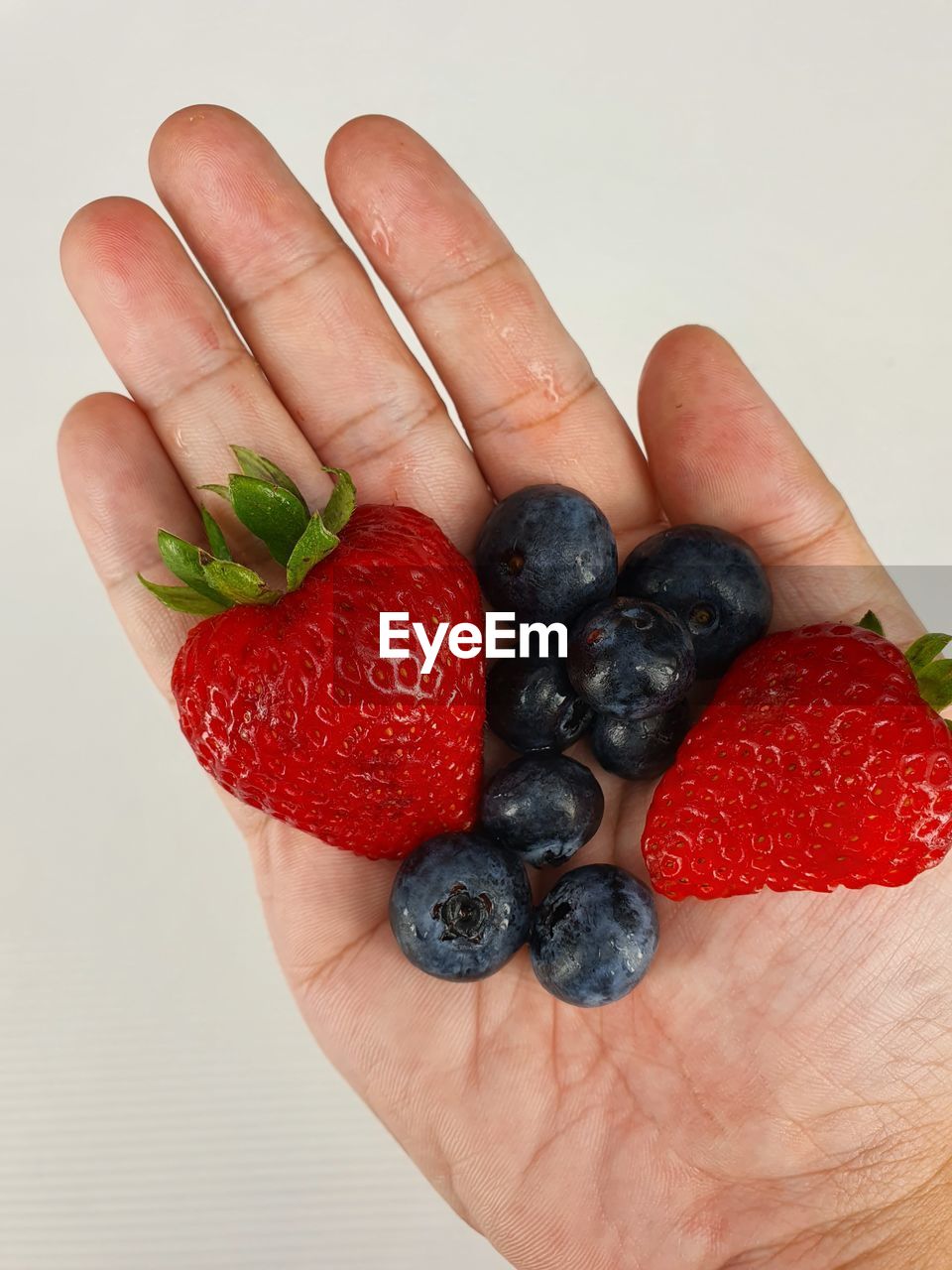 CLOSE-UP OF HAND HOLDING RASPBERRIES