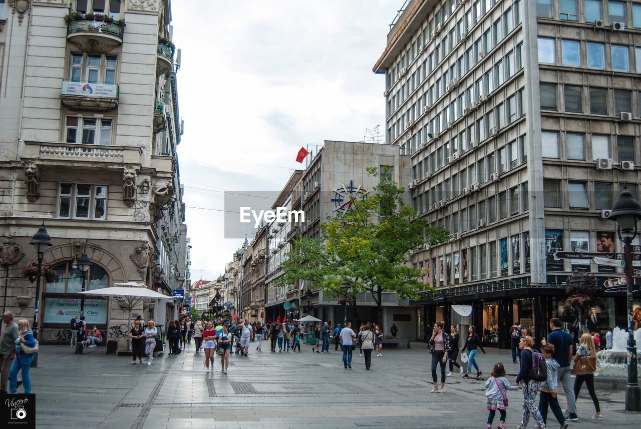 GROUP OF PEOPLE WALKING ON STREET AGAINST BUILDINGS