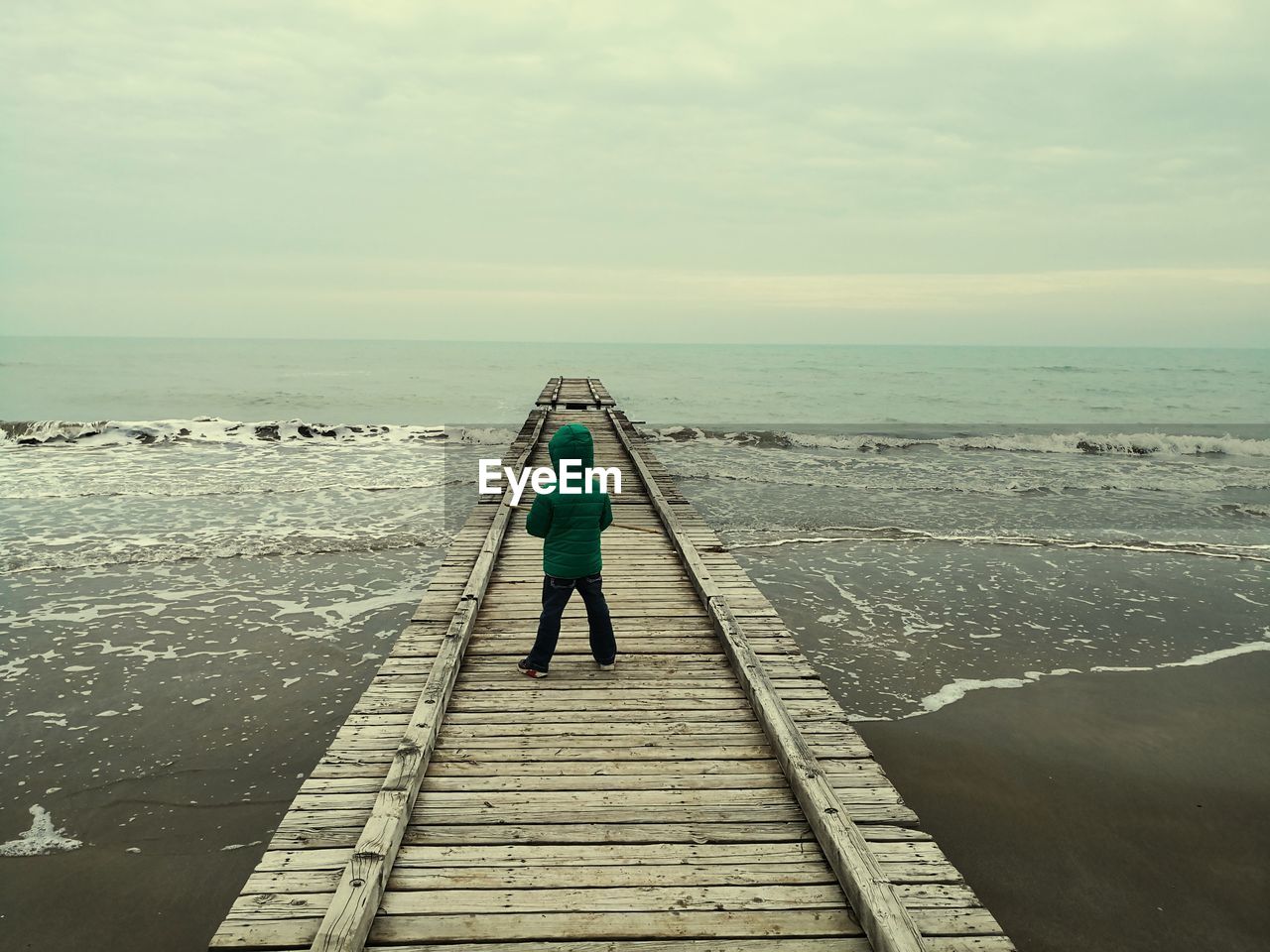 Rear view of boy standing on pier over sea