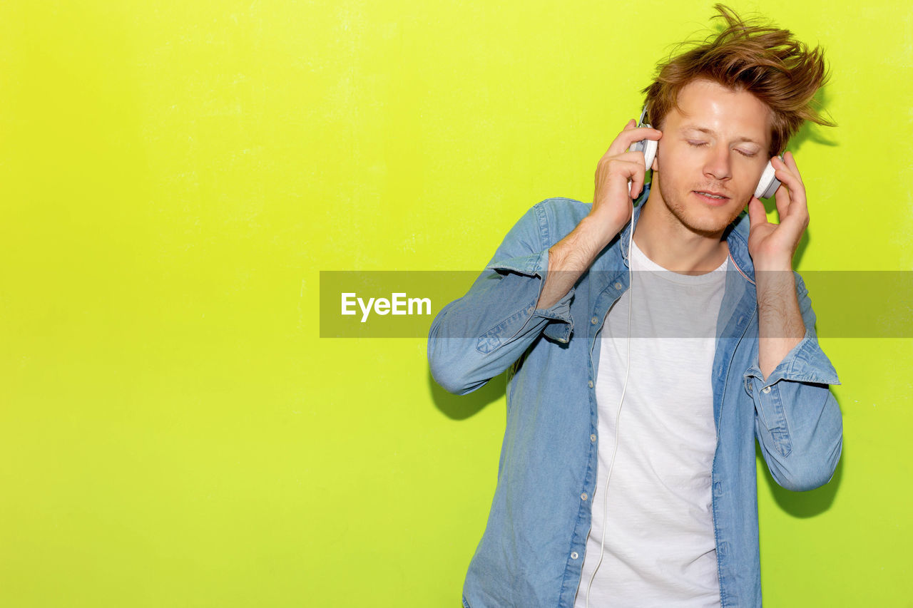 Mid adult man listening to music through headphones against yellow background