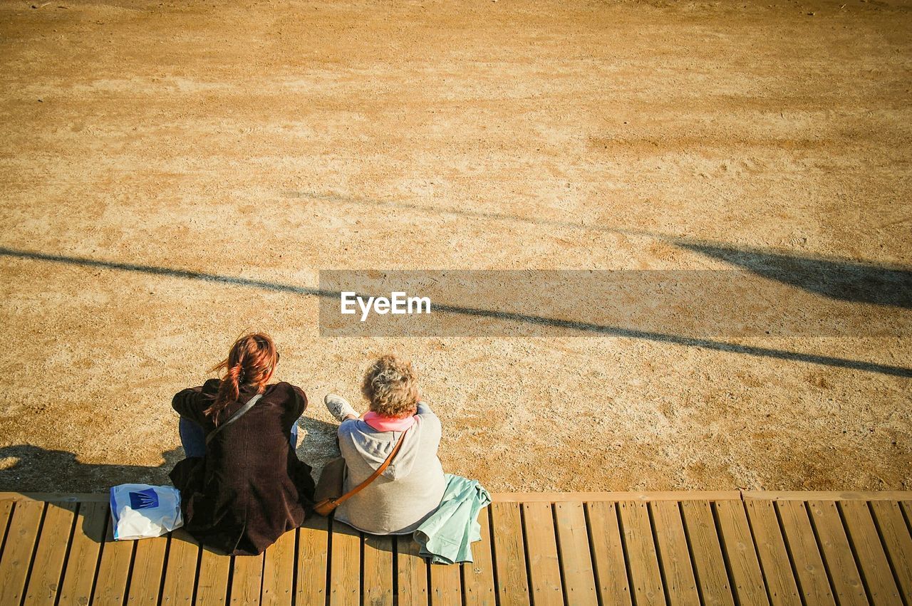 High angle view of friends sitting on boardwalk against field during sunny day