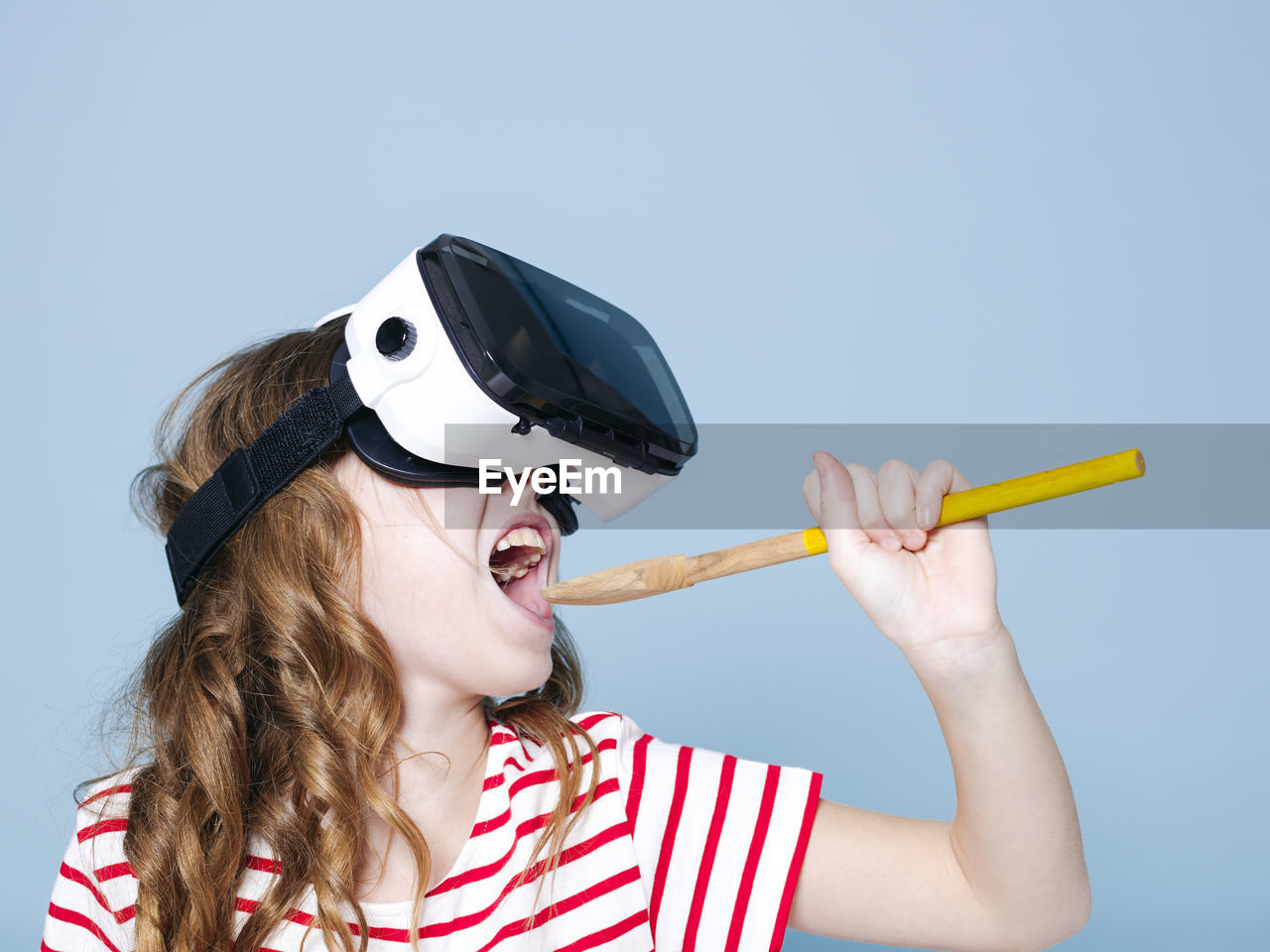 Happy girl holding wood while wearing virtual reality simulator against blue background