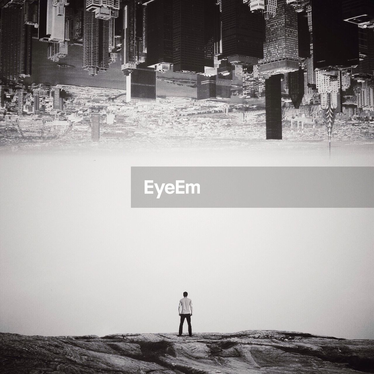 Digital composite image of cityscape above man standing on rocks