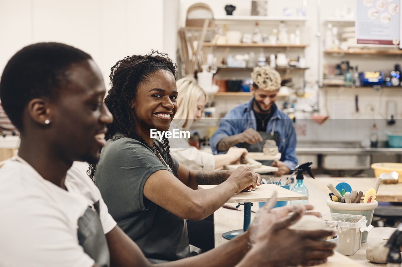 Portrait of smiling woman molding clay sitting by man in art class