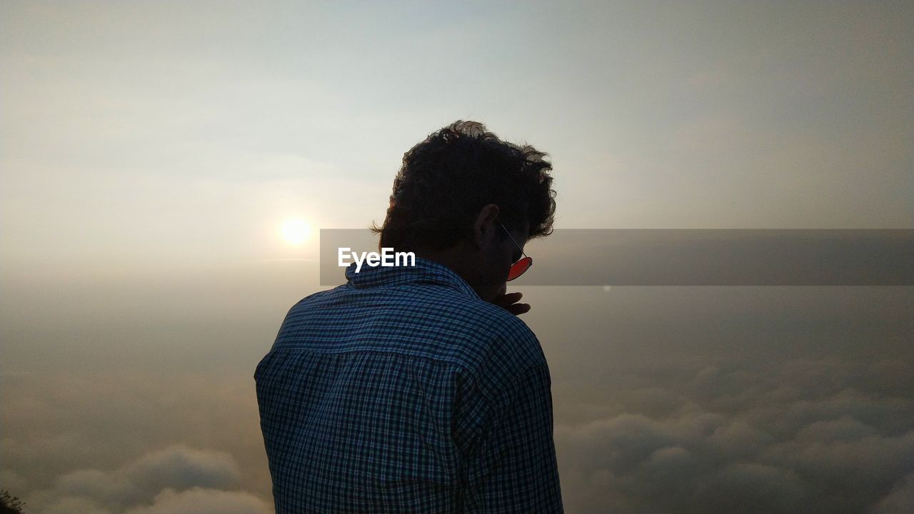 Rear view of man wearing sunglasses against sky during sunset