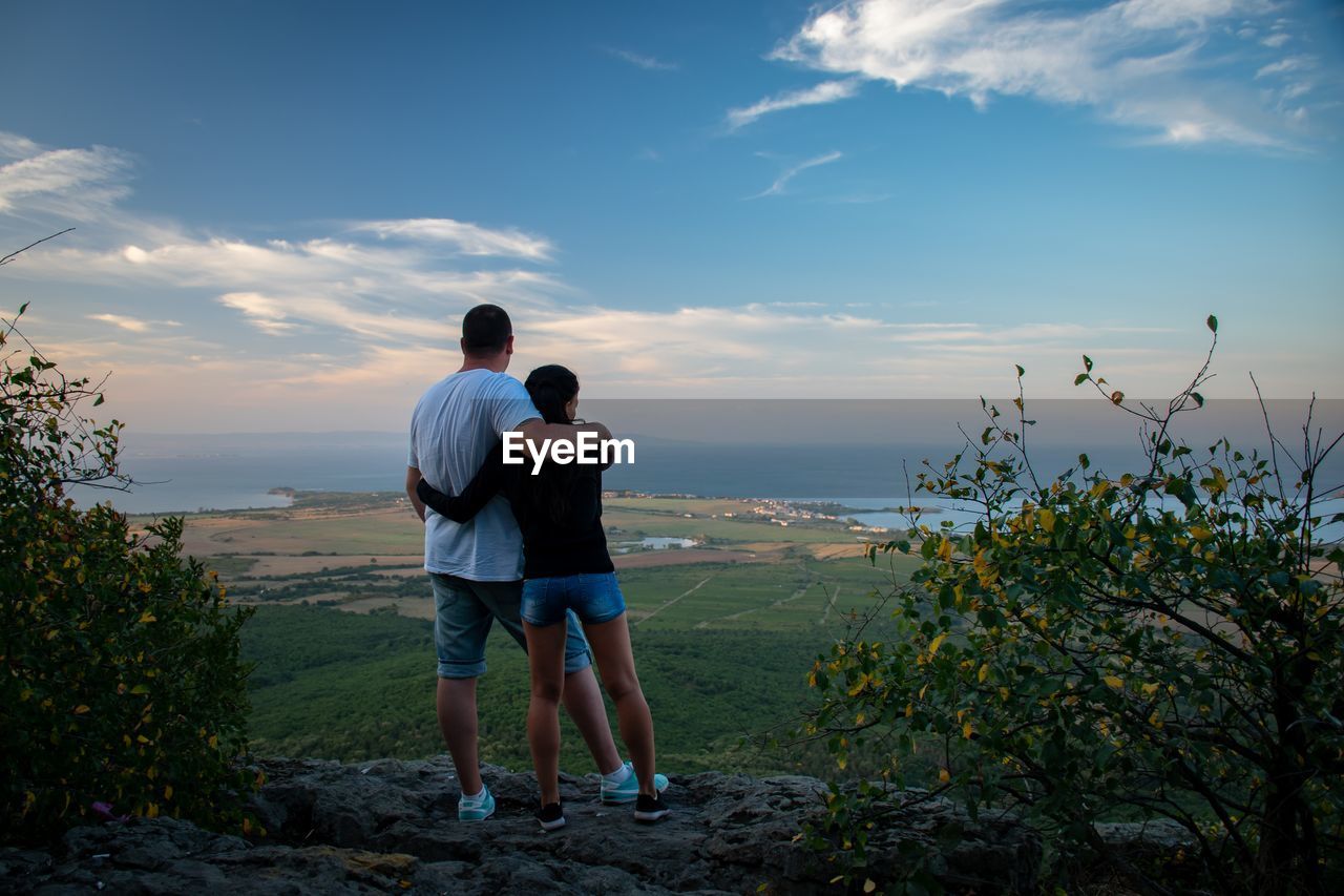 Rear view of couple standing with arms around against landscape