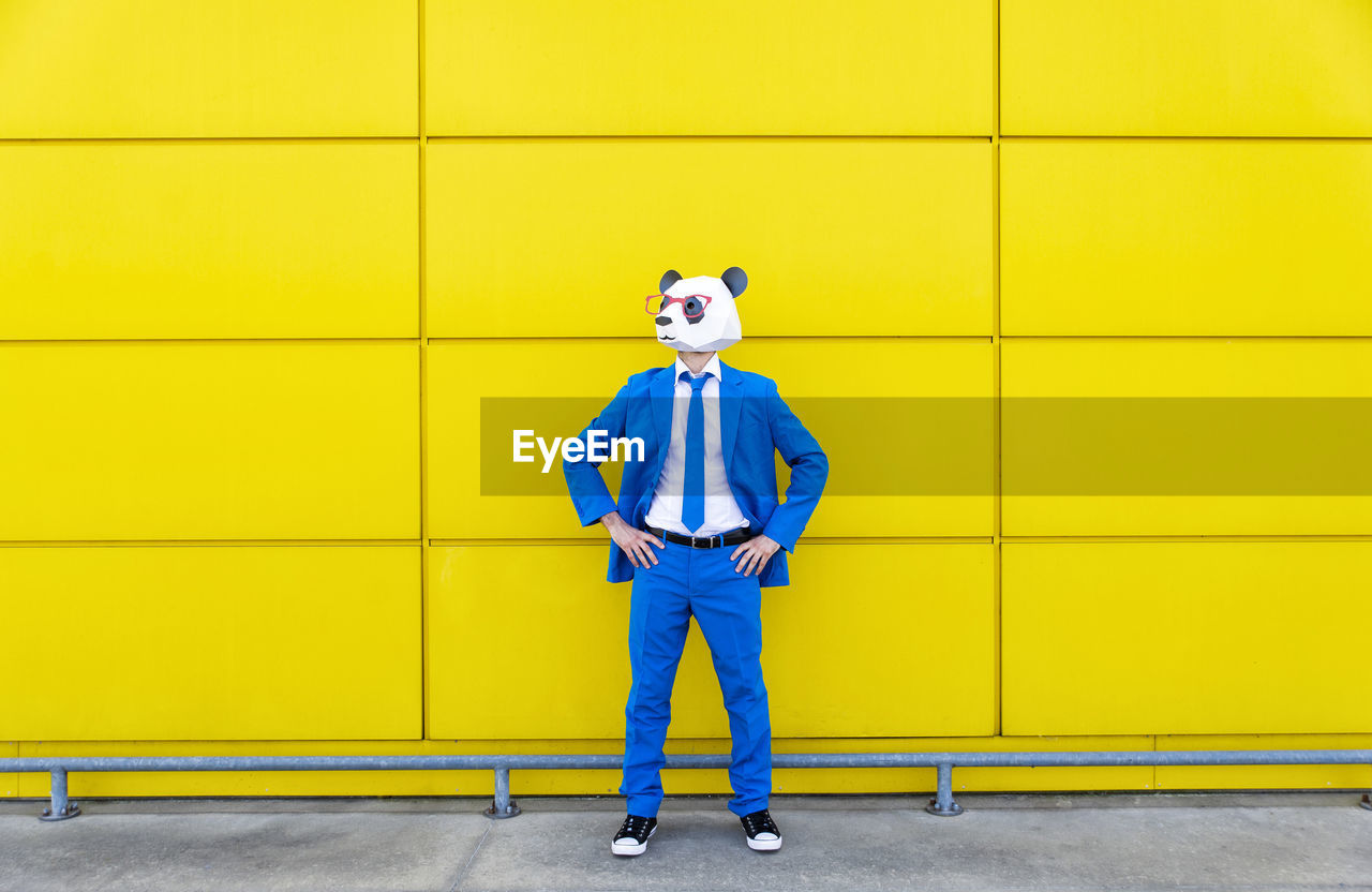 Man wearing vibrant blue suit and panda mask standing in front of yellow wall