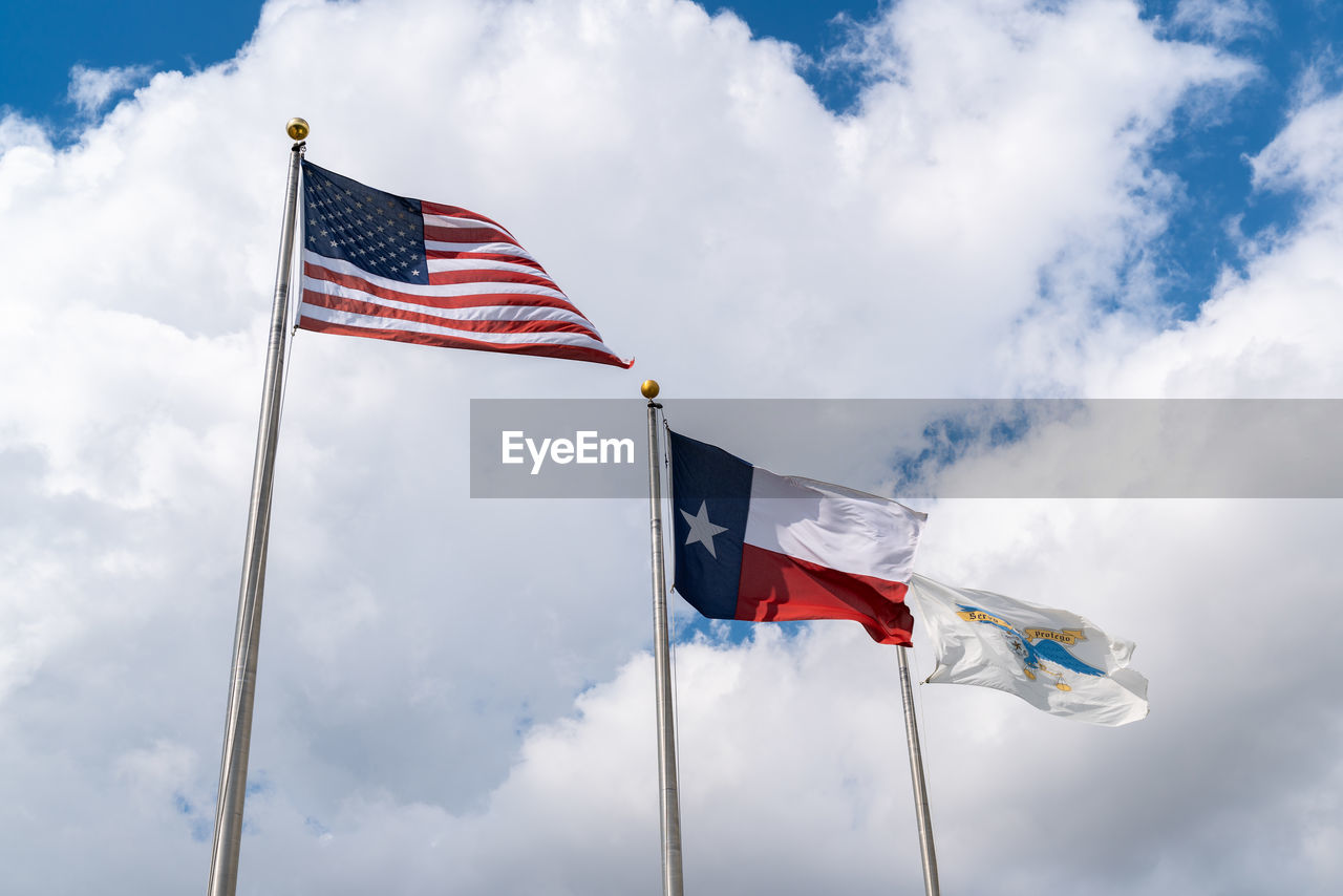 Low angle view of flags waving against cloudy sky