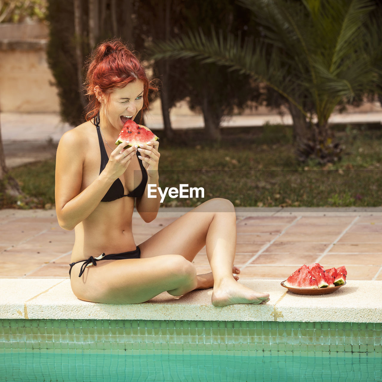 Young woman eating fruits by swimming pool