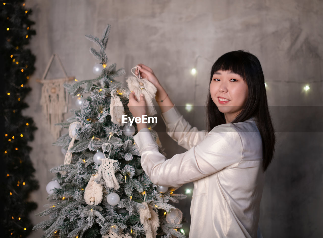 A young, beautiful korean asian woman dresses up a christmas tree with toys 