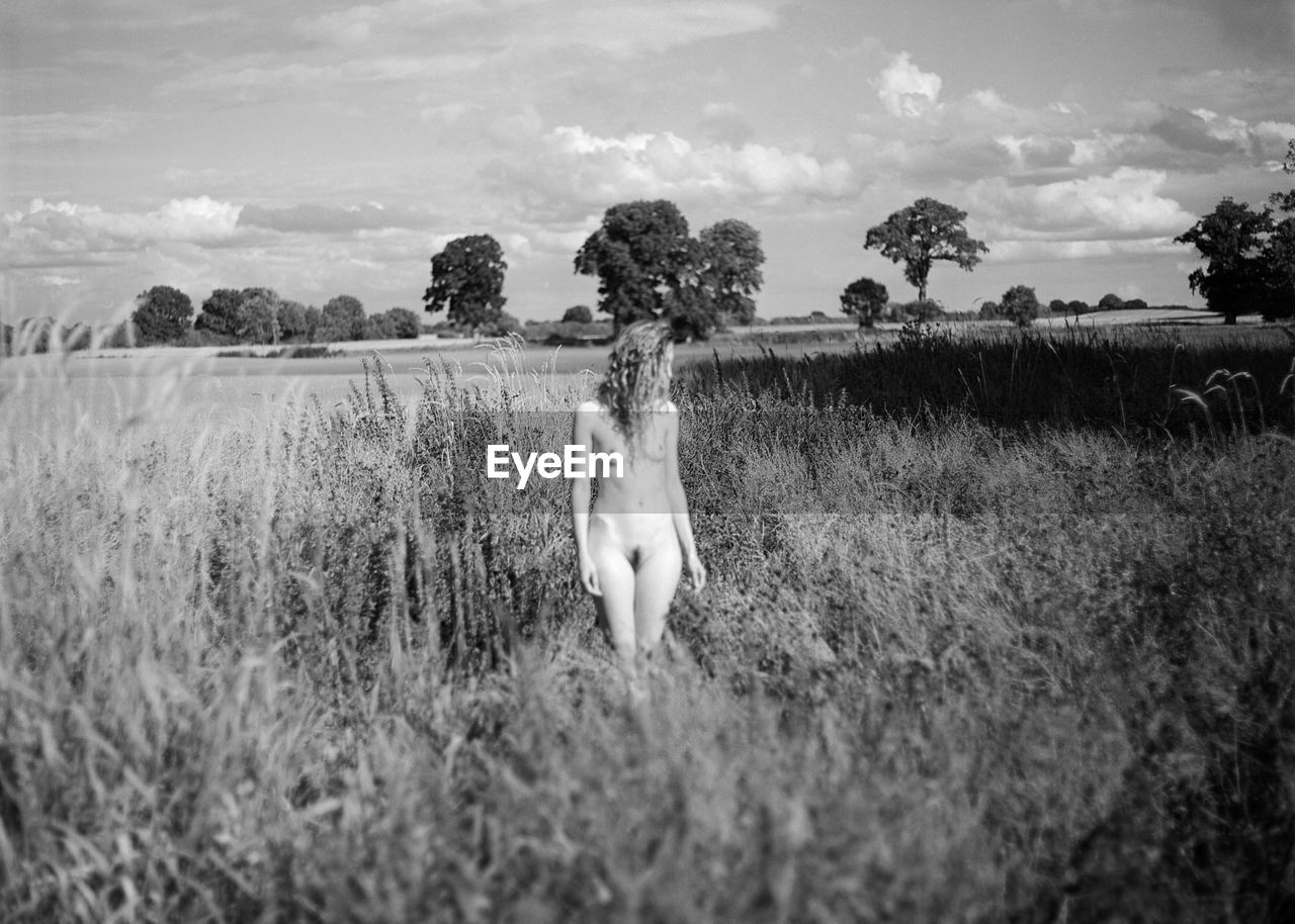 Naked woman standing on field against sky