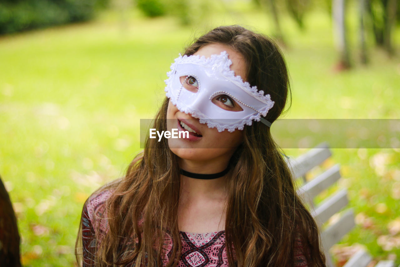 Smiling young woman wearing venetian mask at park