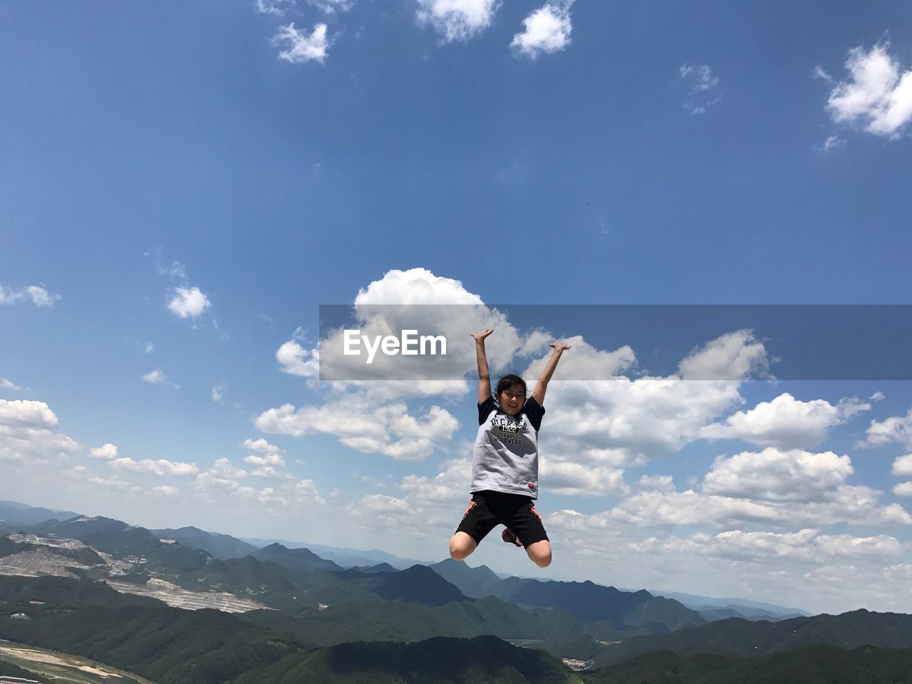 Girl with arms raised jumping against sky during sunny day