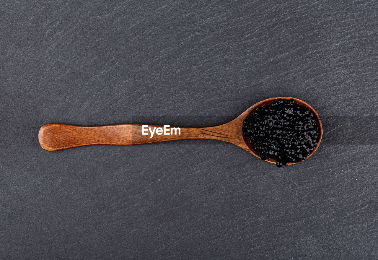 Top view of a wooden spoon with black caviar over a stone serving board.
