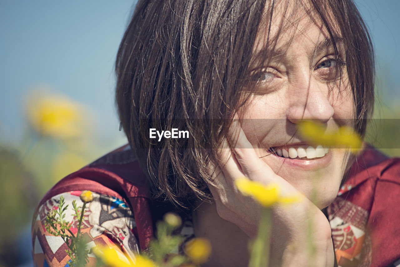 Portrait of woman smiling while lying amidst yellow flowers on field