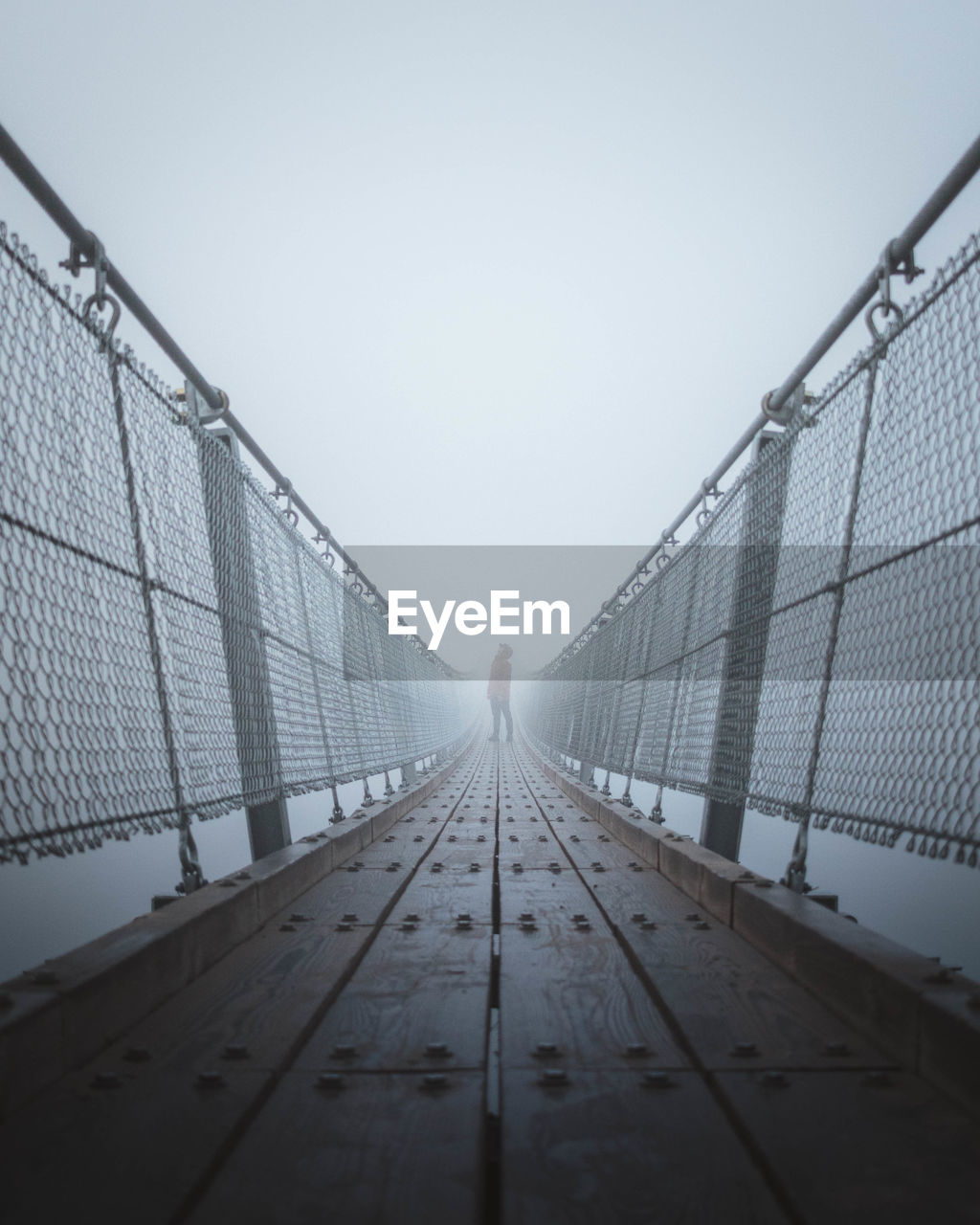 Man standing on footbridge against sky