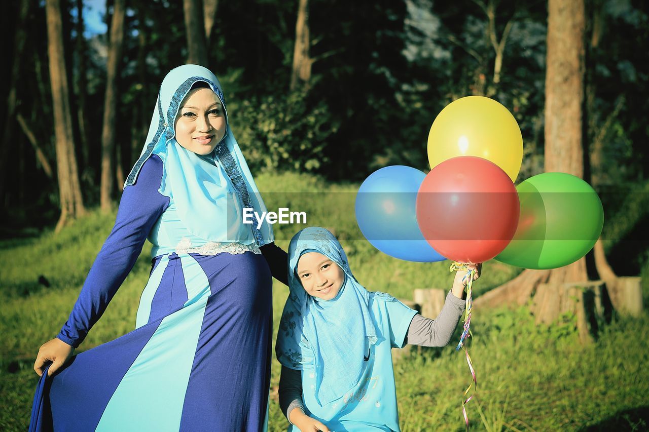 Portrait of pregnant mother with daughter standing in park