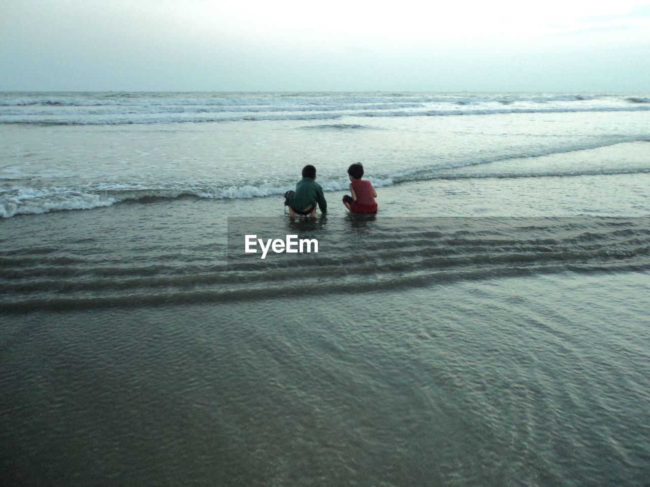 Rear view of boy and girl at beach against sky