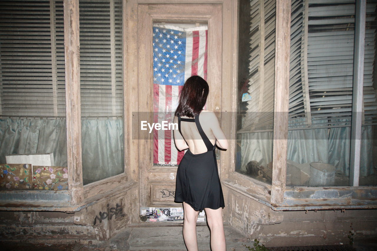 FULL LENGTH REAR VIEW OF WOMAN STANDING AGAINST WINDOW