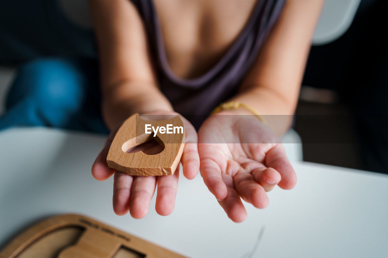 A child is holding a wooden puzzle with a heart shape.