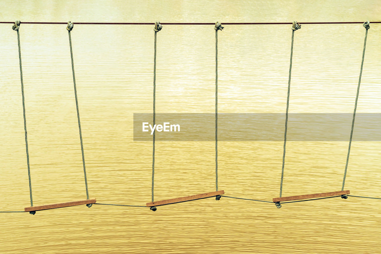 Many swings made of wooden board and tied with rope hang on cable over a small stream flowing 