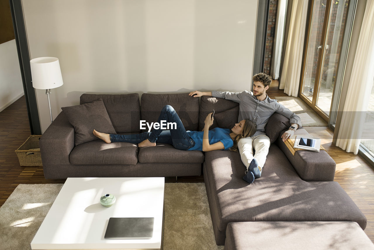 Couple with tablet and smartphone relaxing on sofa in modern living room at home