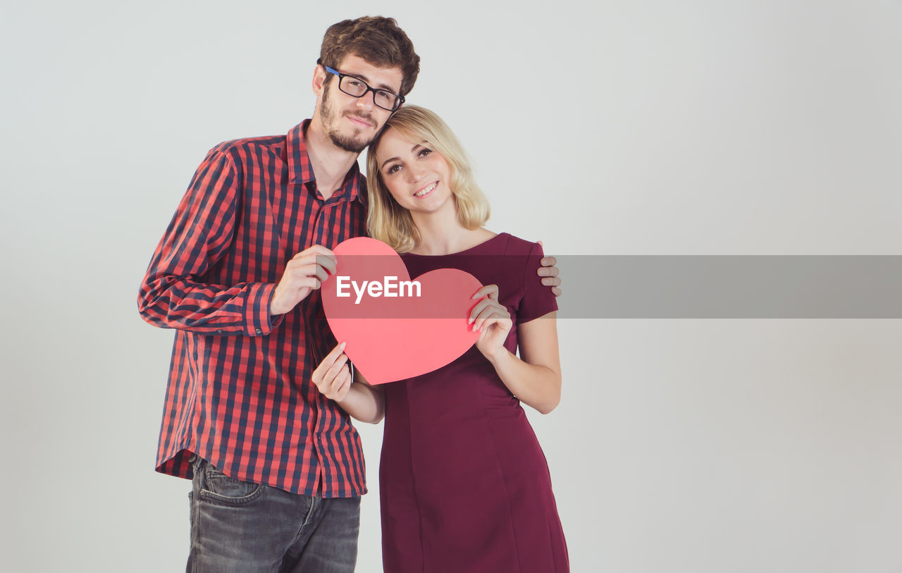 YOUNG COUPLE HOLDING HEART SHAPE ON WHITE BACKGROUND