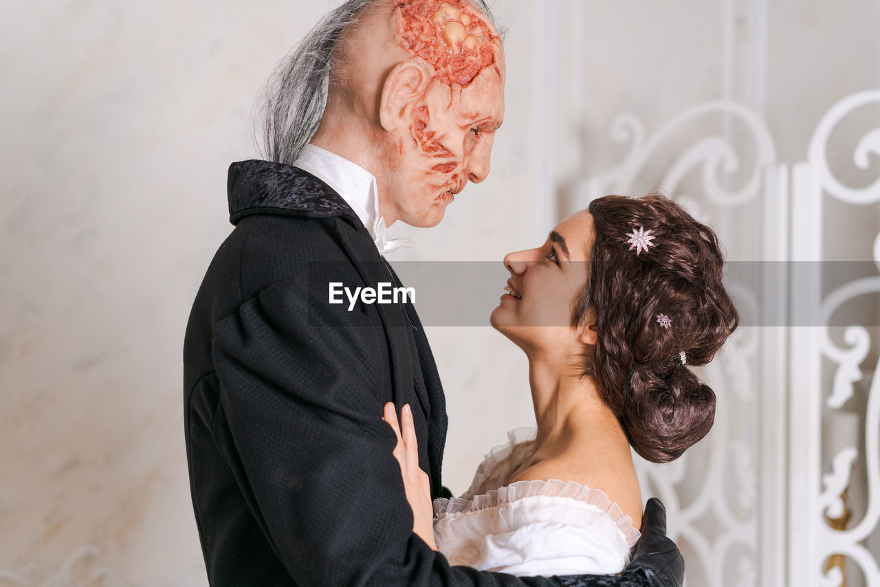 Beautiful girl in white dress and scary disfigured man in black stand