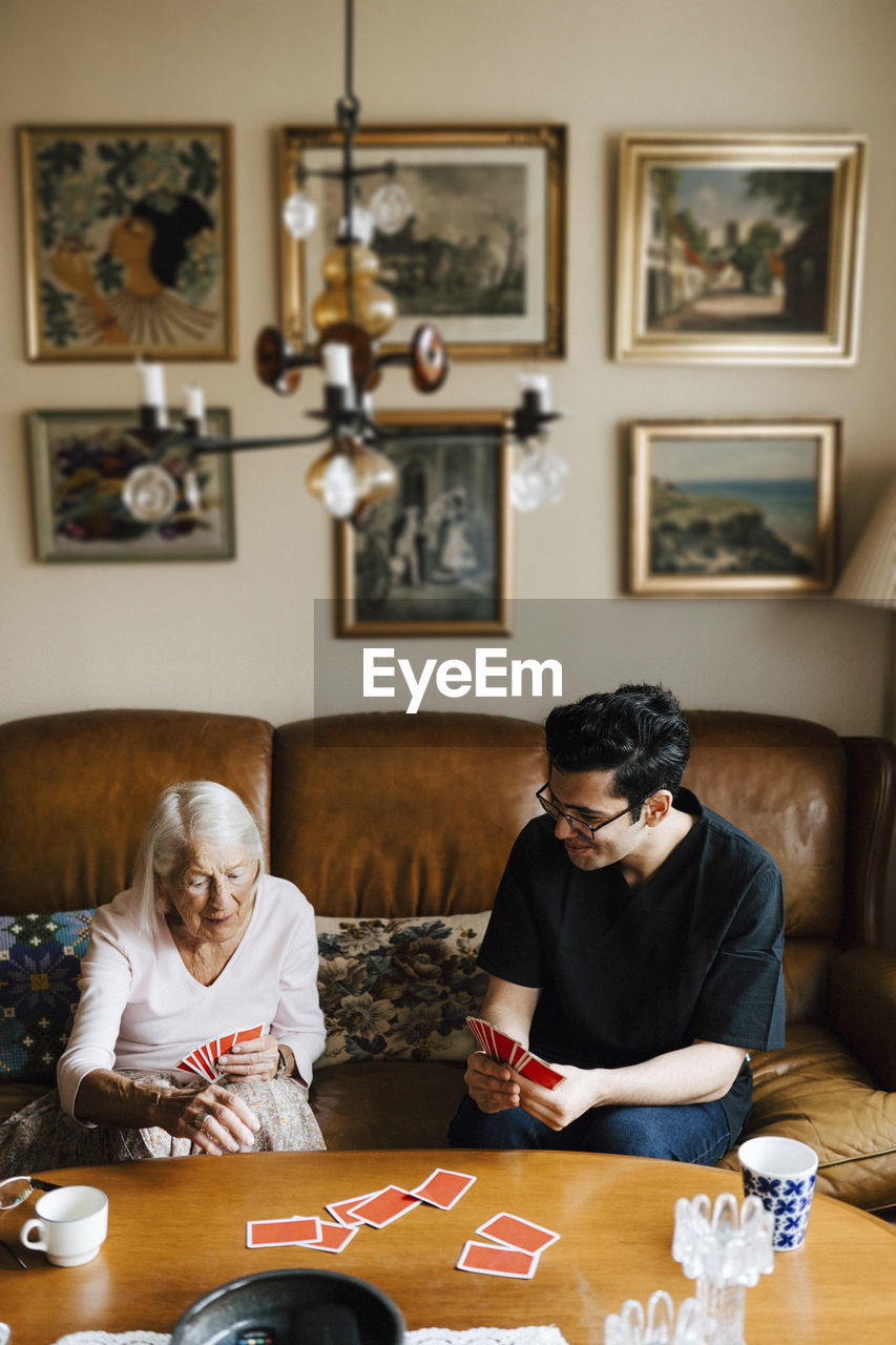 Elderly woman playing cards with male caregiver at table in living room